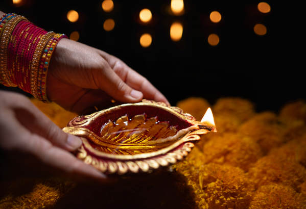 pair of hands holds holding a brass diya that is lit