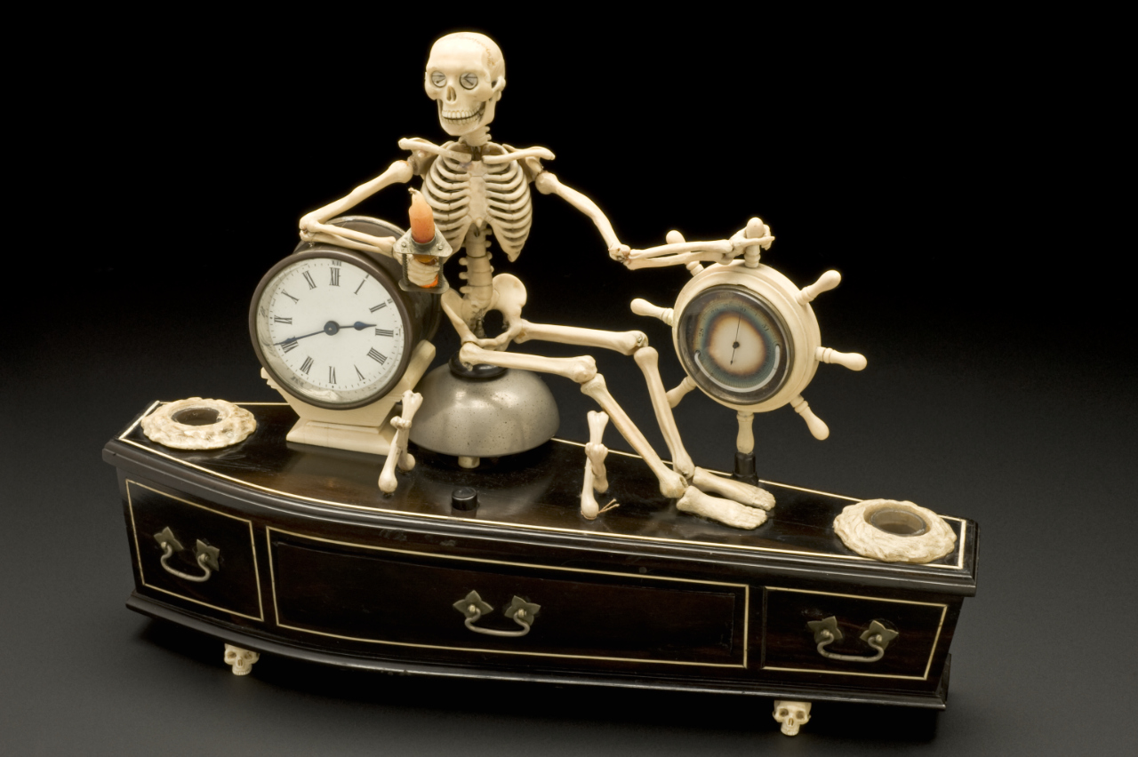 sculpture of a skeleton sitting atop a black coffin which integrates a clock