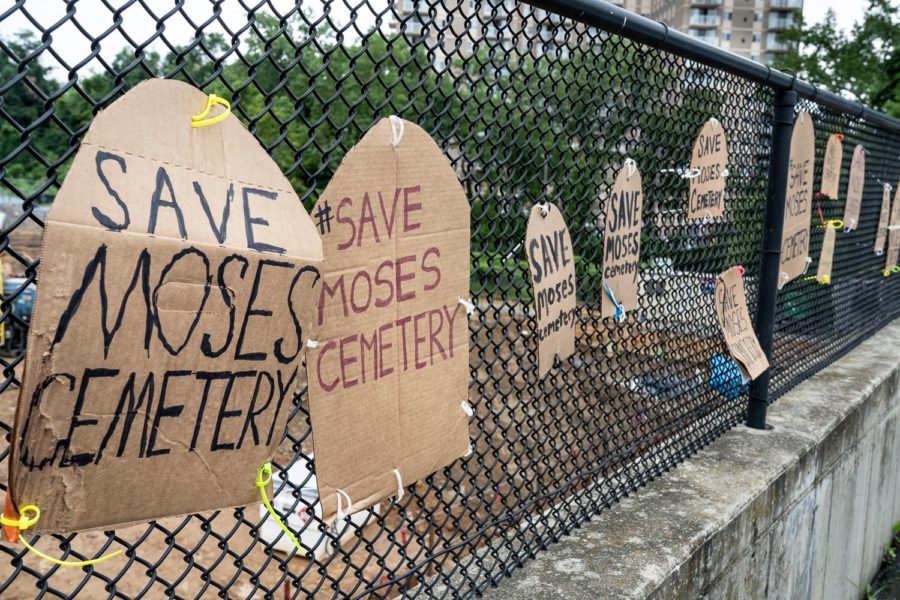 Cardboard tombstones are mounted on a chainlink fence with the words 